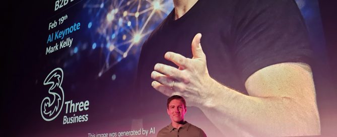 Mark Kelly Innovation and AI Speaker, standing at the stage with a large screen stating the talk track for his keynote about innovation and AI for Three Ireland.