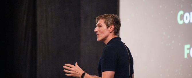 Mark Kelly presenting on stage during a conference with a headset microphone. AI Keynote Speaker 2026