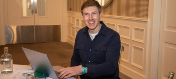 Mark Kelly AI smiling while working on a laptop at a conference table in a meeting room. Nadella's Learning Loop
